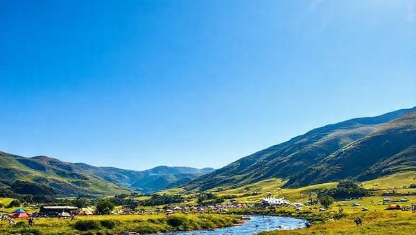 A breathtaking high definition image of the Gore District in New Zealand, showcasing the vibrant summer landscape with lush green pastures under a clear blue sky, dotted with colorful music festival tents. In the foreground, a serene Mataura River flows, with anglers casting their lines, framed by rolling hills. The scene should capture the lively atmosphere and cultural richness of the area, with diverse visitors enjoying outdoor activities, all bathed in warm, golden sunlight.