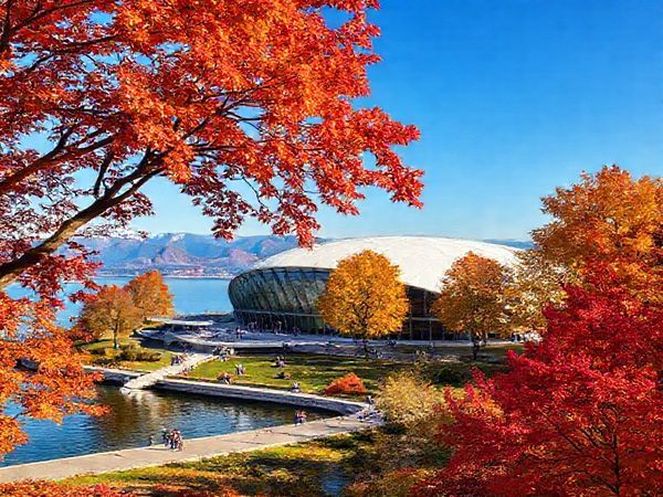 A stunning scene depicting the Zeppelin Museum nestled on the shores of Lake Constance during a vibrant autumn day. Show the museum's architecture surrounded by trees in shades of red, orange, and gold, with visitors leisurely exploring the exhibits and enjoying the beautiful outdoors. Include a glimpse of the lake reflecting the colorful foliage and distant mountains under a clear blue sky. Make the image in high definition.