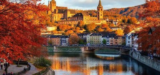"An enchanting view of Heidelberg, Germany, showcasing the stunning Heidelberg Castle and the Neckar River, surrounded by vibrant autumn foliage in hues of orange, red, and gold. Include charming medieval architecture and people enjoying a leisurely stroll along the riverbank. Incorporate a soft golden light of early evening, enhancing the magical atmosphere. Render this scene in high definition."
