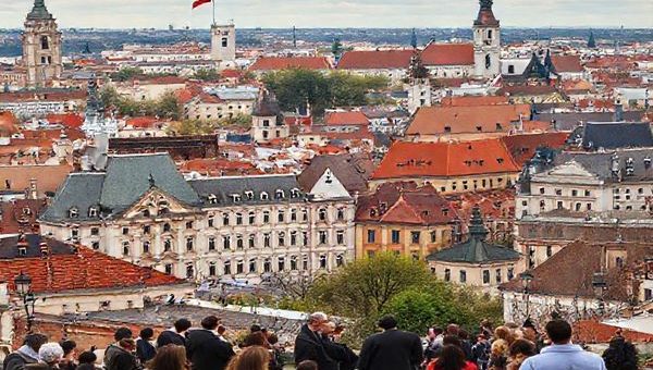 A high-definition image depicting the transformative landscape of the Czech Republic post-1989, showcasing a vibrant cityscape blending historical architecture with modern business buildings. Visual elements include diverse groups of people engaged in discussions, emphasizing the fusion of Western ethical concepts with Czech cultural identity. The background should feature symbols of integration into the European Union and NATO, like flags or emblems, reflecting the journey of evolving business ethics. The atmosphere should convey a sense of optimism and growth as the society grapples with its past and looks towards a future rooted in ethical practices.