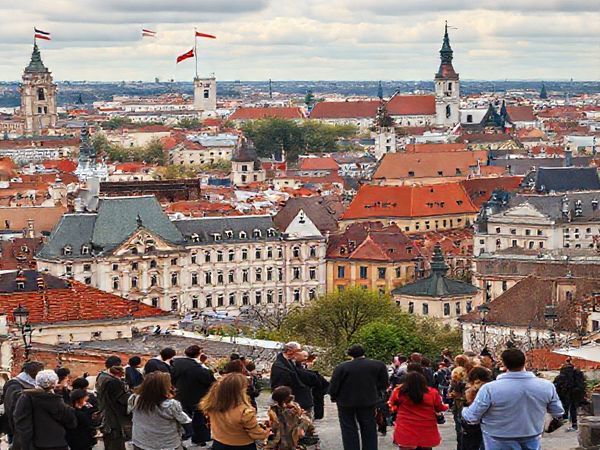 A high-definition image depicting the transformative landscape of the Czech Republic post-1989, showcasing a vibrant cityscape blending historical architecture with modern business buildings. Visual elements include diverse groups of people engaged in discussions, emphasizing the fusion of Western ethical concepts with Czech cultural identity. The background should feature symbols of integration into the European Union and NATO, like flags or emblems, reflecting the journey of evolving business ethics. The atmosphere should convey a sense of optimism and growth as the society grapples with its past and looks towards a future rooted in ethical practices.