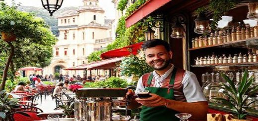 A vibrant Italian café scene adorned with rich green and red colors, featuring a smiling barista serving espresso to travelers, with historic architecture and lush landscapes in the background. Incorporate musical notes symbolizing Italian opera and artwork inspired by Michelangelo subtly integrated into the surroundings. The atmosphere is warm and inviting, capturing the essence of Italian culture and the joy of language learning. High definition.
