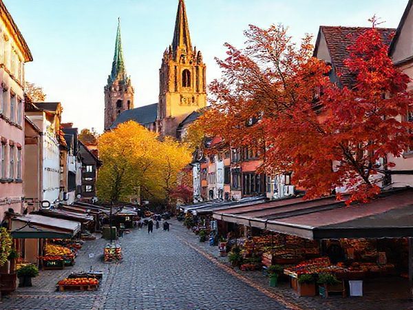 A picturesque view of Wittenberg, Germany, during autumn, showcasing cobblestone streets lined with medieval architecture adorned in vibrant shades of gold and crimson leaves. The scene captures local markets bustling with fresh produce, while an iconic church stands in the background, bathed in the soft glow of early evening light. High-definition.
