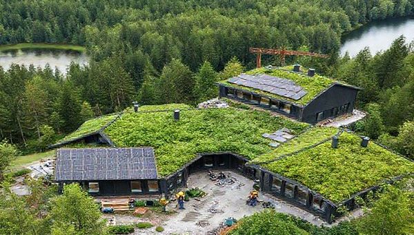 A high-definition image of a lush, green Swedish construction site, integrating innovative sustainable building materials and technologies. Scenic views of forests and water bodies surround modern eco-friendly structures, showcasing solar panels and green roofs. Include workers collaborating on-site, with charts and KPIs visible in the foreground, symbolizing the blend of nature and construction efficiency while capturing Sweden's commitment to sustainability.