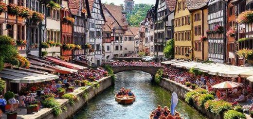 A vibrant summer scene in Tübingen, showcasing the lively atmosphere with cobbled streets lined with medieval architecture and bustling cafes. Capture the annual punting boat race on the glistening Neckar River, with colorful crowds enjoying picnics along the banks. Include blooming flowers and lush greenery, and ensure the image reflects the warmth and charm of this enchanting university town in high definition.