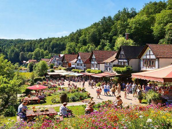 A vibrant summer scene in Landkreis Anhalt-Bitterfeld, Germany, showcasing lush green forests and charming traditional villages under a bright blue sky. Include picnic areas by tranquil lakes, sun-kissed fields filled with wildflowers, and cheerful locals enjoying outdoor festivals. The atmosphere should be lively and inviting, capturing the essence of a warm summer day. High definition.
